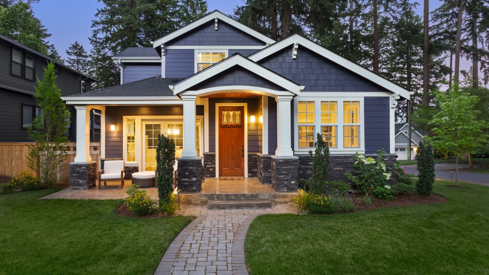Craftsman-style house with blue siding, white trim, and glowing windows at dusk