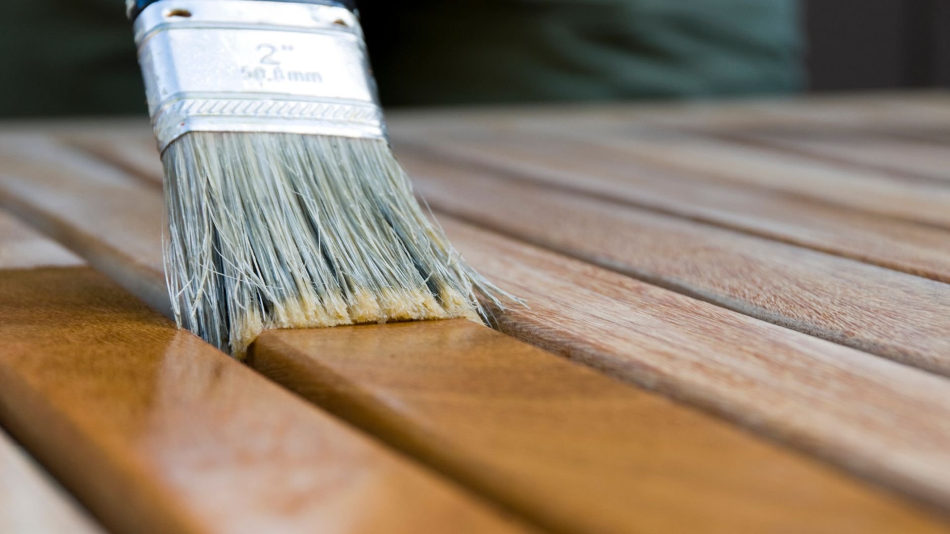Paintbrush applying stain or varnish on wooden deck or furniture surface