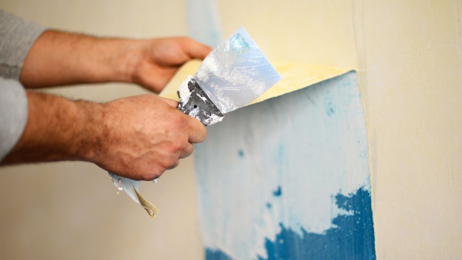 Hand using putty knife to repair and smooth wall surface