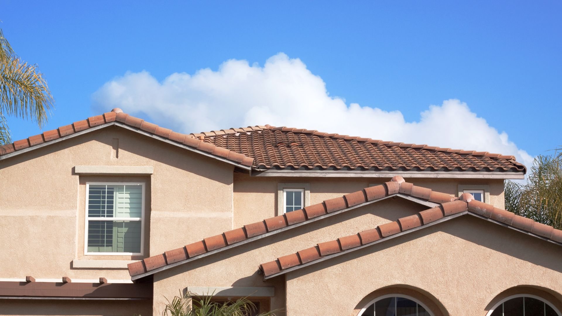 Stucco house with terracotta tile roof under blue sky with clouds